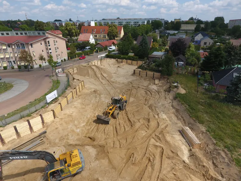 Radlader und Bagger beim Aushub einer großen Baugrube mit Verbau
