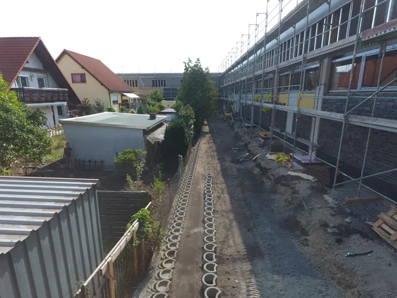 Leitungsgraben mit Schachtringen entlang eines Bestandsgebäudes