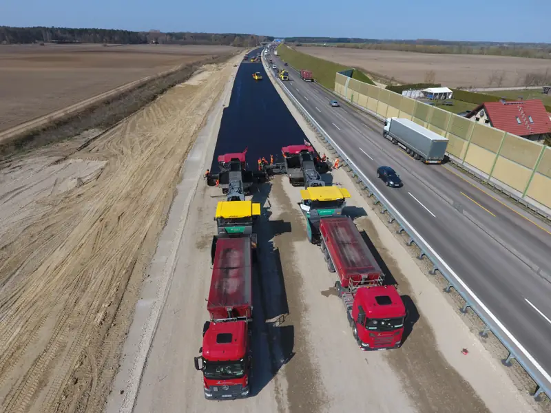 Asphaltfertiger und Lkw beim Straßenbau auf einer Autobahn bei Berlin