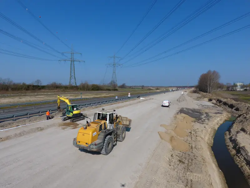 Radlader und Bagger beim Erdbau neben einer Autobahn